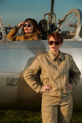 Aviation. Two professional female commercial aviation pilots in uniform and sunglasses posing on the airfield with their fighter jet ready to start their flight. 