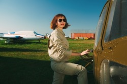 Portrait of a smiling professional helicopter pilot with bright red lips and black sunglasses posing by her aircraft before the flight. 