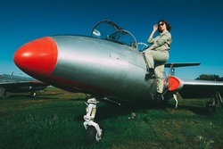 Beautiful pilot woman in a uniform and sunglasses getting on her fighter jet to start the flight. Military and commercial aircraft. Full length portrait in the background of an airfield and a blue sky