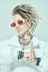 Portrait of a confident stylish punk rock musician with dreadlocks posing in a white suit and sunglasses on a light background. Youth alternative culture. Cybepunk style. 