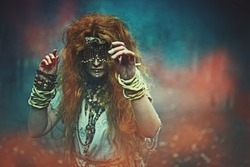 A frightening forest witch with a mask on her eyes doing a mysterious ritual in a dark gloomy forest. Woman shaman. Paganism. Death ritual. Halloween. 