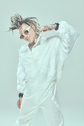 Modern stylish punk rock musician with dreadlocks posing joyfully smiling in white suit and white sunglasses on a light background. Youth alternative culture. Futuristic space and cybepunk style. 