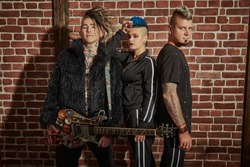 Youth alternative culture. Cool group of punk rock musicians with stylish mohawks posing in black concert costumes against a brick wall. Grunge style. 