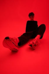 Full length shot of a moody handsome guy in fashionable youth clothes sitting on a bright red background. Fashionable youth fashion. Youth problems and emotions.