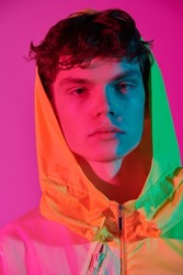 Fashionable youth style. Portrait of a cool guy posing in a bright yellow jacket with a hood on his head. Bright pink background. Creative designer clothes. Close up portrait.