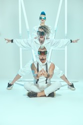Group of punk rock musicians in white overalls and cool cyber glasses posing at the studio in neon light. Youth alternative culture. Full length shot.
