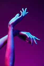 Photo of graceful thin hands with sparkling silvery skin in bright neon blue and purple lighting. Body painting, body art. Glitter makeup. Beauty industry, cosmetology.