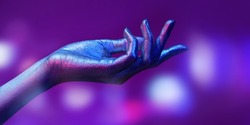 Close-up photo of a beautiful hand with sparkling silvery skin in bright neon blue and pink lighting. Body painting, body art. Glitter makeup. Beauty industry, cosmetology. 