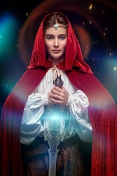 A young prince of elves in a red velvet cloak and a crown stands with a sword in his hands. Studio shot on a black background with lights and sparks. Fairy tale, magic. Fantasy.