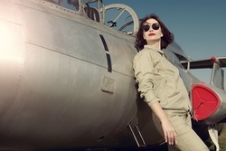 Military and commercial aircraft. Portrait of a confident pilot woman wearing uniform and sunglasses posing next to her fighter jet. 