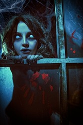 Horror scene. A scary ghost girl looks out of the window of an old abandoned house. Haunted house. Halloween.