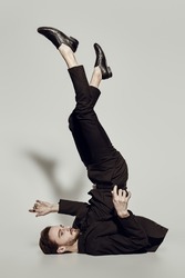 A man in elegant black suit and shoes lies on the floor with his legs raised up. Fashion shot. 