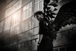 A male Black Angel stands at sunset in front of an old concrete building. Place for text. The concept of war, doomsday, Apocalypse.