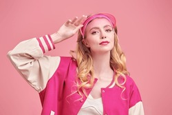 Pink color and femininity style in fashion. A cute blonde girl posing in a fashionable pink bomber jacket and a visor cap on a pink studio background. Youth fashion.