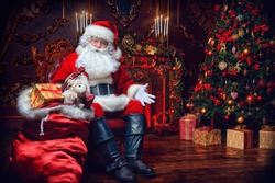 Surprised Santa Claus in a beautiful room next to the fireplace and Christmas tree sits with a sack of gifts . 