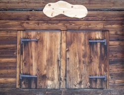 Wooden facade of a mountain hut  with closed window shutters and empty plate for content