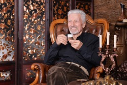 Portrait of smiling senior man drinking coffee at home while sitting in vintage chair