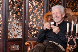 Smiling senior man drinking coffee at home while sitting in vintage chair