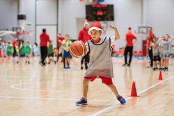 Young boy with Santa Clause hat exercises with a basketball ball in a sports hall