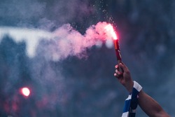 Football fan burns flare in the hand with scarf at the stadium
