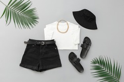 White t-shirt, black denim shorts, flat sandals, bucket hat, gold chain necklace on grey background. Women's outfit. Trendy stylish summer look. Fashion clothes, flat lay.