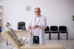 Old male doctor with skeleton in the clinic