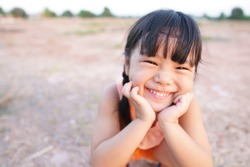 Asian children cute or kid girl smile with laugh and happy fun because come back home to country and wear traditional top or sleeveless shirt sit on arid soil for agriculture at home