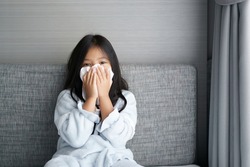 Asian child or kid girl sick and runny nose sneezing or snot with cold cough on tissue paper covering nose from influenza or coronavirus covid-19 and allergy weak from PM 2.5 dust at hospital or home