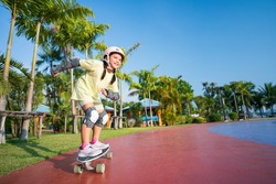 asian child or kid girl smile playing surf skate or skateboard in skatepark and extreme sports exercise to wearing helmet elbow pads wrist and knee support for body safety protect at bang phra park
