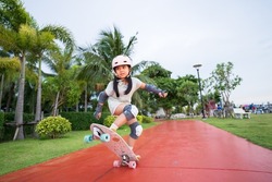 asian child skater or kid girl playing skateboard or surf skate and ollie jumping fun or raise wheel manual in skate park by extreme sports to wear helmet elbow pads wrist knee support for body safety