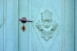 Old vintage door hardware on a green door with ornate coffered panel.