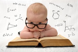 funny portrait of cute baby in glasses lying on old book and thinking of all the knowledge in the world