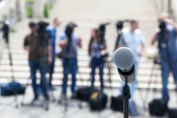 Microphone in focus against blurred camera operators and journalists. Press conference.