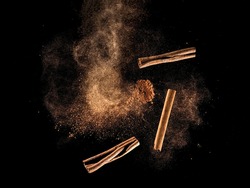 Cinnamon powder and sticks explosion on black background