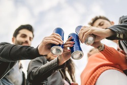 Group of young people toasting with canned beers. View from bottom, focus on the cans.