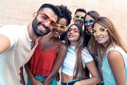 Group of teenagers taking a funny selfie wearing weird colorful sunglasses. Young people having fun using smart phones.