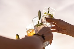 Friends rising cocktail glasses for a celebratory toast against the sky in the summer