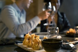 Restaurant table with Dim Sum, Traditional Chinese dumplings, in the foreground. Defocused in the background a couple of young people are drinking white wine. Concept of fusion food and wine.