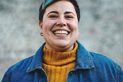 carefree young cheerful androgenic looking person with toothy smile close-up looking at camera - really confident hipster style person with piercing isolated on blurred background - body positives