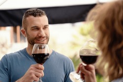 A man in sharp focus enjoys a glass of red wine, sharing a special moment with his partner, subtly visible in the foreground.