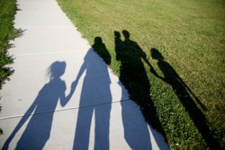 Shadows of a family of five walking in the park holding hands