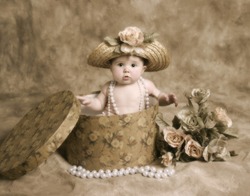 Portrait of an adorable baby girl playing dress up, sitting in a hatbox wearing a straw hat and pearl necklace