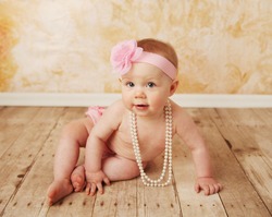 Adorable young baby girl wearing a vintage pearl necklace and pink rose headband