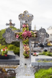 old stone grave cross decorated with ceramic flowers on a cemetery