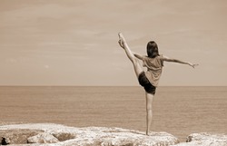 caucasian girl performing rhythmic gymnastics exercises with the leg up and the foot over the head by the sea with Sepia Effect