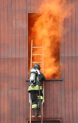 firefighter in action in the fire station with self-contained breathing apparatus and oxygen cylinders during the rescue drill and the thick orange smoke coming out of the window