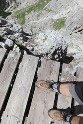 hiking boots of hiker walking on a suspended wooden bridge over the dolomites high mountain precipice of the european alps