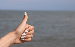hand of young girl with thumbs up  by the sea