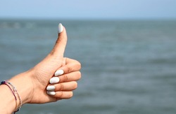 hand of young girl with thumbs up  by the sea