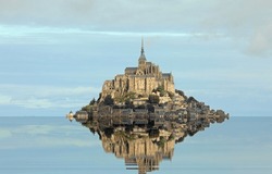 Reflected on the water at high tide of the Hill with the ancient abbey of Mont Saint Michel in Normandy in Northern France and the blue sky
